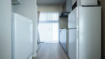 Una cocina estrecha con electrodomésticos blancos, una ventana con cortinas ligeras y suelo de madera.