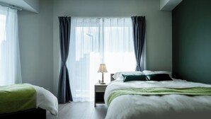 Une chambre d’hôtel avec deux lits, une table de chevet et une fenêtre avec des rideaux légers.