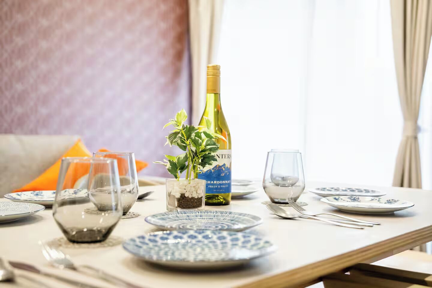 A dining table set with plates, glasses, and a bottle of wine.