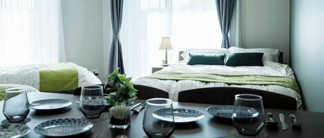 A hotel room with two beds, a dining table set with plates, glasses, and cutlery, and a lamp on a bedside table.