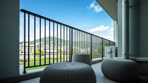 Un balcon offrant une vue sur le paysage urbain et les montagnes, agrémenté de deux poufs ronds en fibres tressées et d’une rambarde en métal noir.