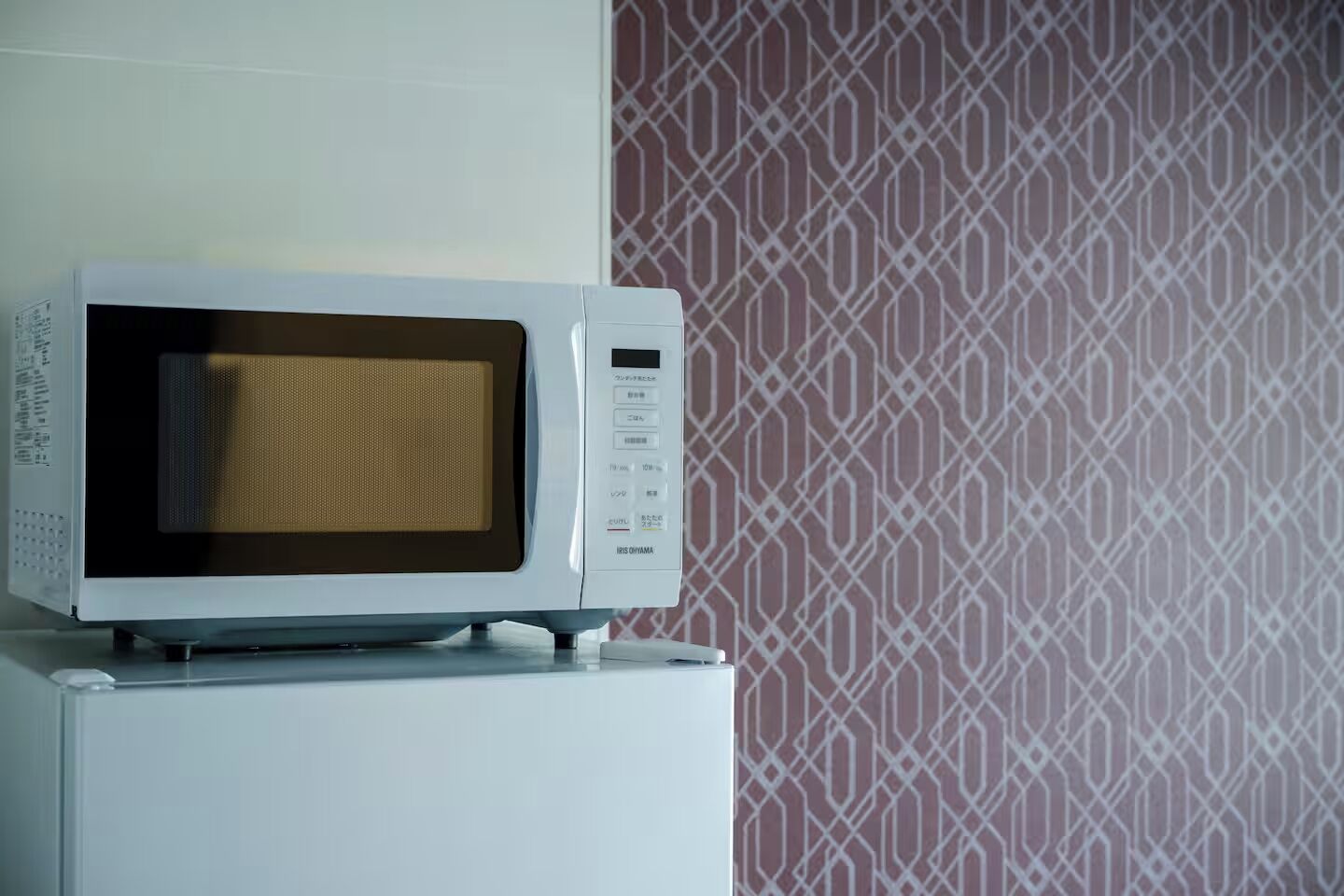 A microwave on a white appliance, possibly a refrigerator, with a patterned wallpaper in the background.