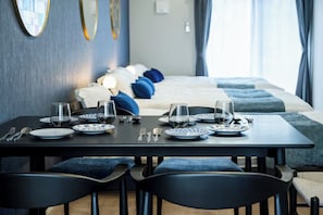 A neatly set dining table with plates, glasses, and cutlery, a bed with blue and white bedding, and a modern room with a blue accent wall and decorative mirrors. - ZEE HAVEN Nagasakiekimae (Nagasaki)
