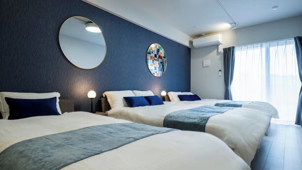 Una habitación de hotel con dos camas, un espejo redondo, un reloj de pared y una ventana con cortinas.