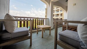A balcony with a wooden table and two cushioned seating areas, overlooking a building with balconies. - Diani Beachfront Paradise (Diani Beach)