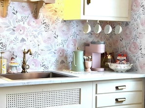 A kitchen with a sink, a coffee maker, a kettle, and a bowl of cereal.