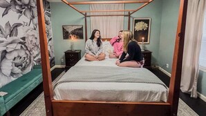 Ein Bett mit Baldachin in einem Zimmer mit floralem Wandpapier, einem Nachttisch und einem gerahmten Bild an der Wand.
