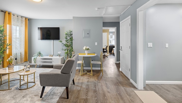 Een moderne woonkamer met een grijze bank, een ronde salontafel en een flatscreen televisie aan de muur.