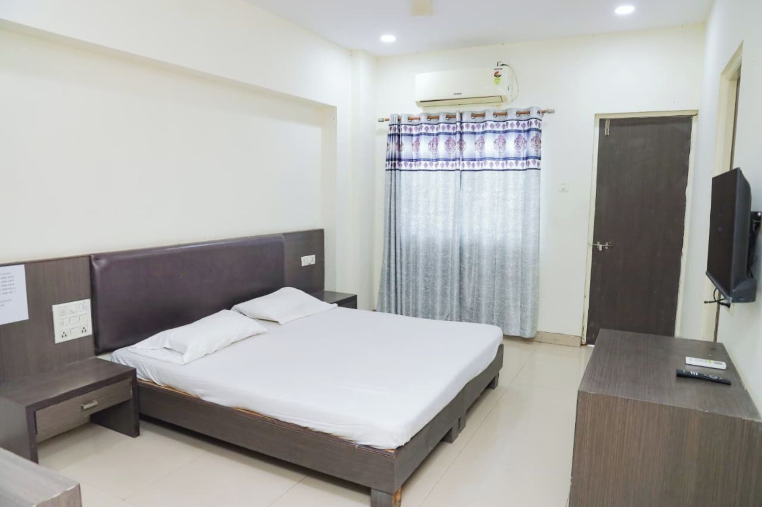 A hotel room with a single bed, a bedside table, a TV, and a wardrobe.