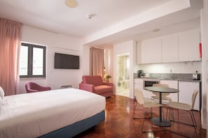 A hotel room with a bed, a desk, a chair, a TV, and a kitchenette. - Lisbon Serviced Apartmentos - Campos (Lisbon)