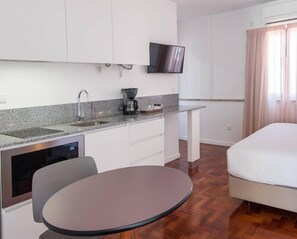 A compact hotel room with a kitchenette, a flat-screen TV, a bed, and a dining table. - Lisbon Serviced Apartmentos - Campos (Lisbon)