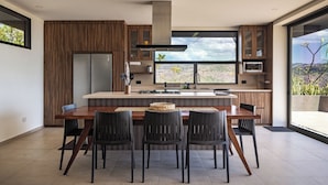 Una cocina moderna con una isla central, sillas oscuras y un ventanal que ofrece vistas al exterior.
