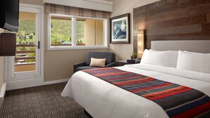 Ein Hotelzimmer mit einem großen Bett, einem Sessel, einem Fenster mit Blick auf eine hügelige Landschaft und einem wandmontierten Fernseher.
