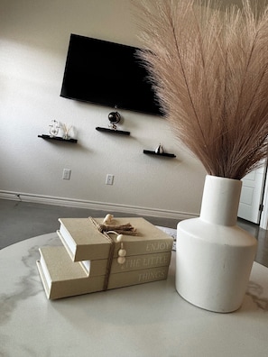 A living room with a flat-screen TV mounted on the wall, a white vase with pampas grass, and a stack of books on a round table. - 14+ day Stay in Killeen- Fully furnished, all utilities, WiFi, security camera (Killeen)