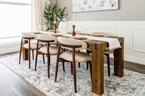 A dining area with a wooden table set for six, surrounded by six chairs with cushioned seats.