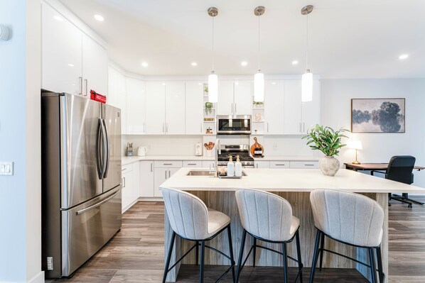 A modern kitchen with white cabinets, stainless steel appliances, and a central island with bar stools.