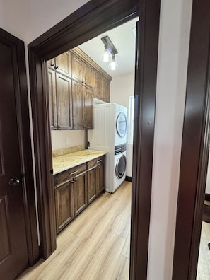 Een wasserette met een wasmachine en droger, houten kastjes en een lichtgekleurd aanrecht.