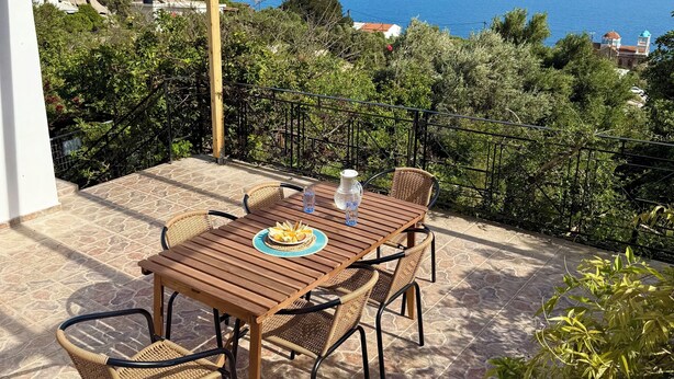 Une table en bois avec des chaises, une vue sur la mer et une structure en forme de pergola.