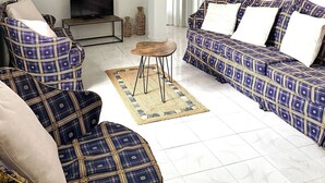 Un salon comprenant un canapé, un fauteuil et une petite table. On y trouve également un téléviseur et des objets décoratifs accrochés au mur.