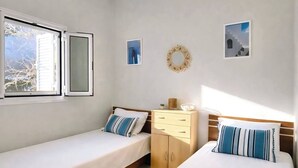 Une chambre avec deux lits simples, une table de chevet en bois, un miroir et une fenêtre avec un volet ouvert.