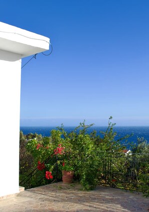 A stone-paved patio with a white structure and a view of the sea.