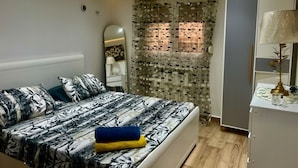 Een slaapkamer met een bed, een kledingkast, een spiegel en een raam met patroon gordijnen.