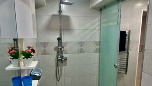 Een badkamer met een douche, een wastafel met spiegel en een toilet. De muren zijn betegeld met decoratieve tegels en er is een klein plankje met toiletartikelen.