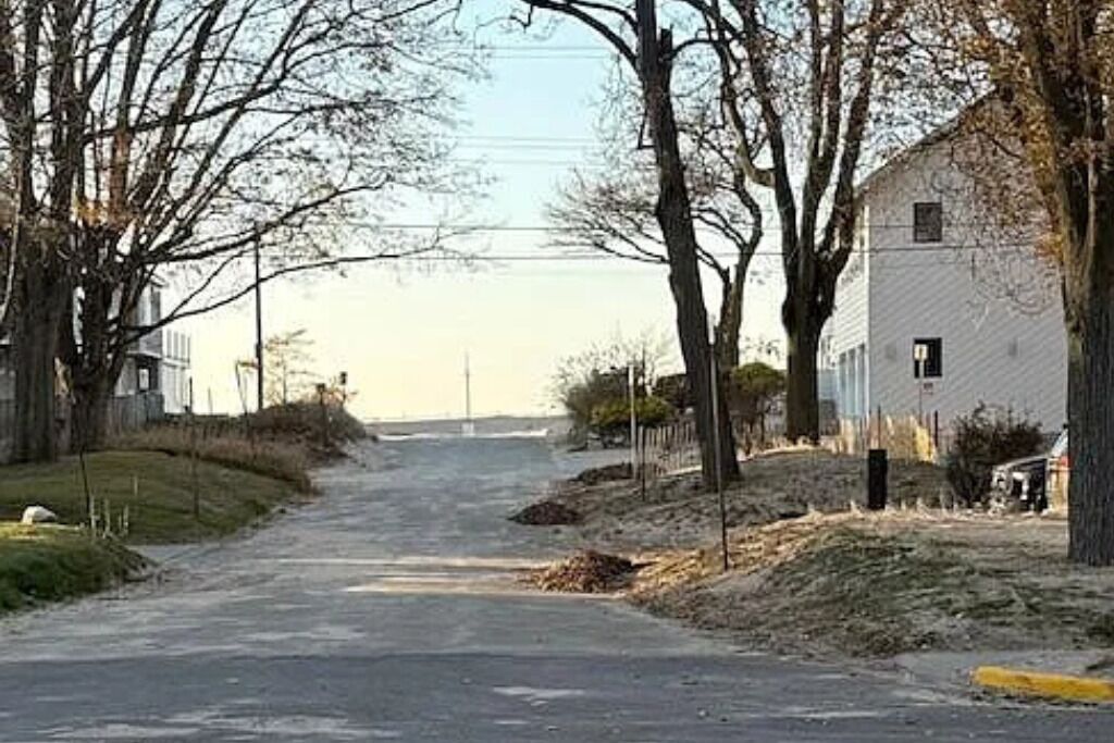 A narrow, tree-lined road leading to a white building with a small porch.