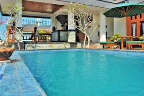 A swimming pool with a stone border, a bar area, and outdoor seating. - D' Artha Cottage (Bali)