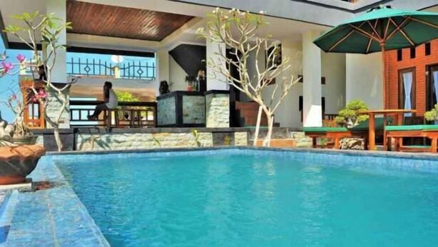 A swimming pool with stone tiles, surrounded by outdoor seating and plants. - D' Artha Cottage (Bali)