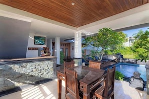 An outdoor dining area with a stone counter, wooden chairs, and a view of a swimming pool. - D' Artha Cottage (Bali)