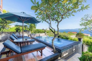 Un espace aménagé au bord de la piscine, avec des chaises longues et une table, entouré de verdure et offrant une vue sur une étendue d’eau.