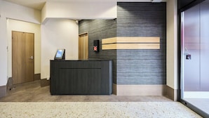 Et receptionsområde med en trædør, en receptionistskranke, en intercom ophængt på væggen og en stor skydedør.