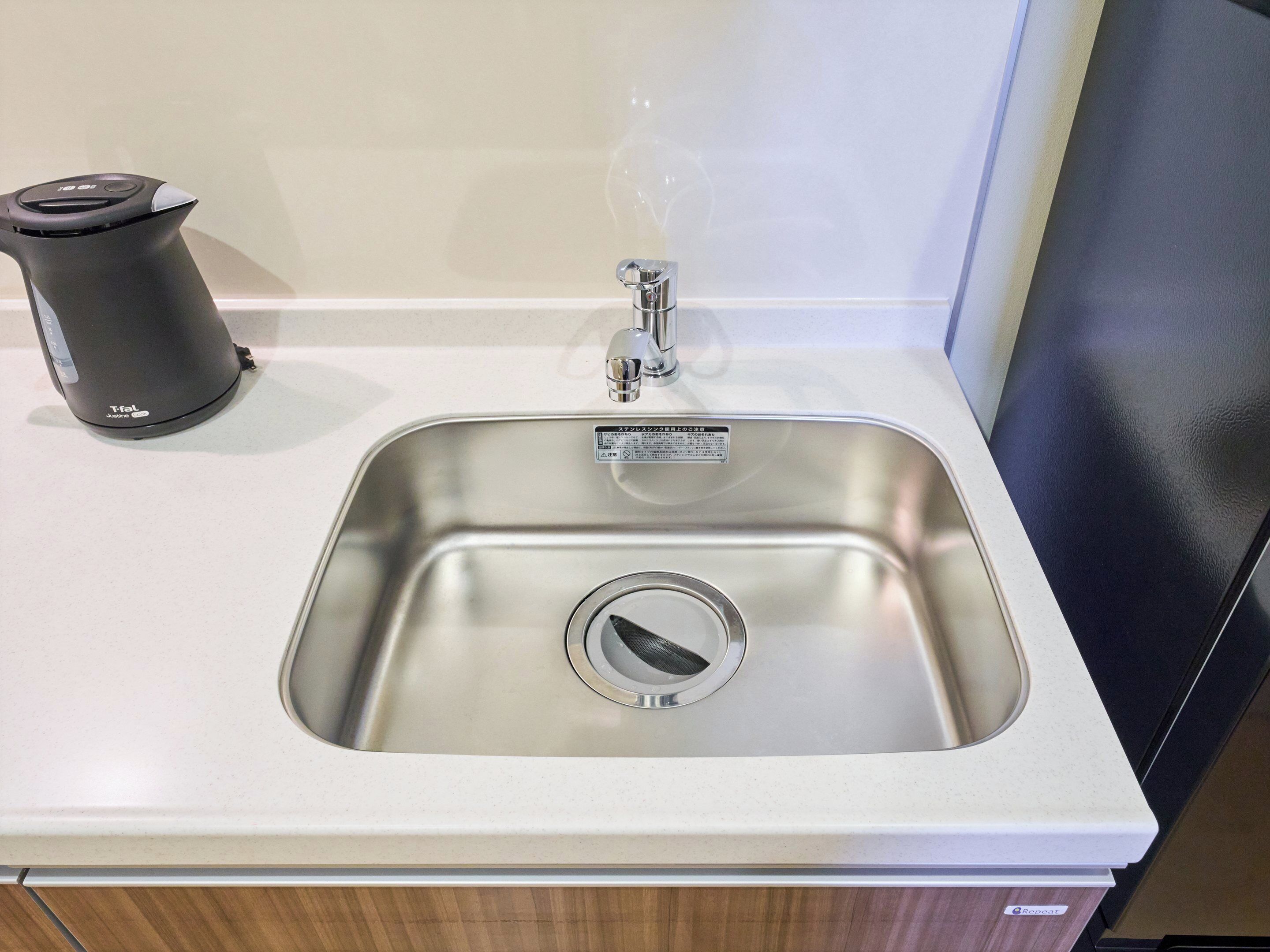 A stainless steel sink with a soap dispenser and a faucet.