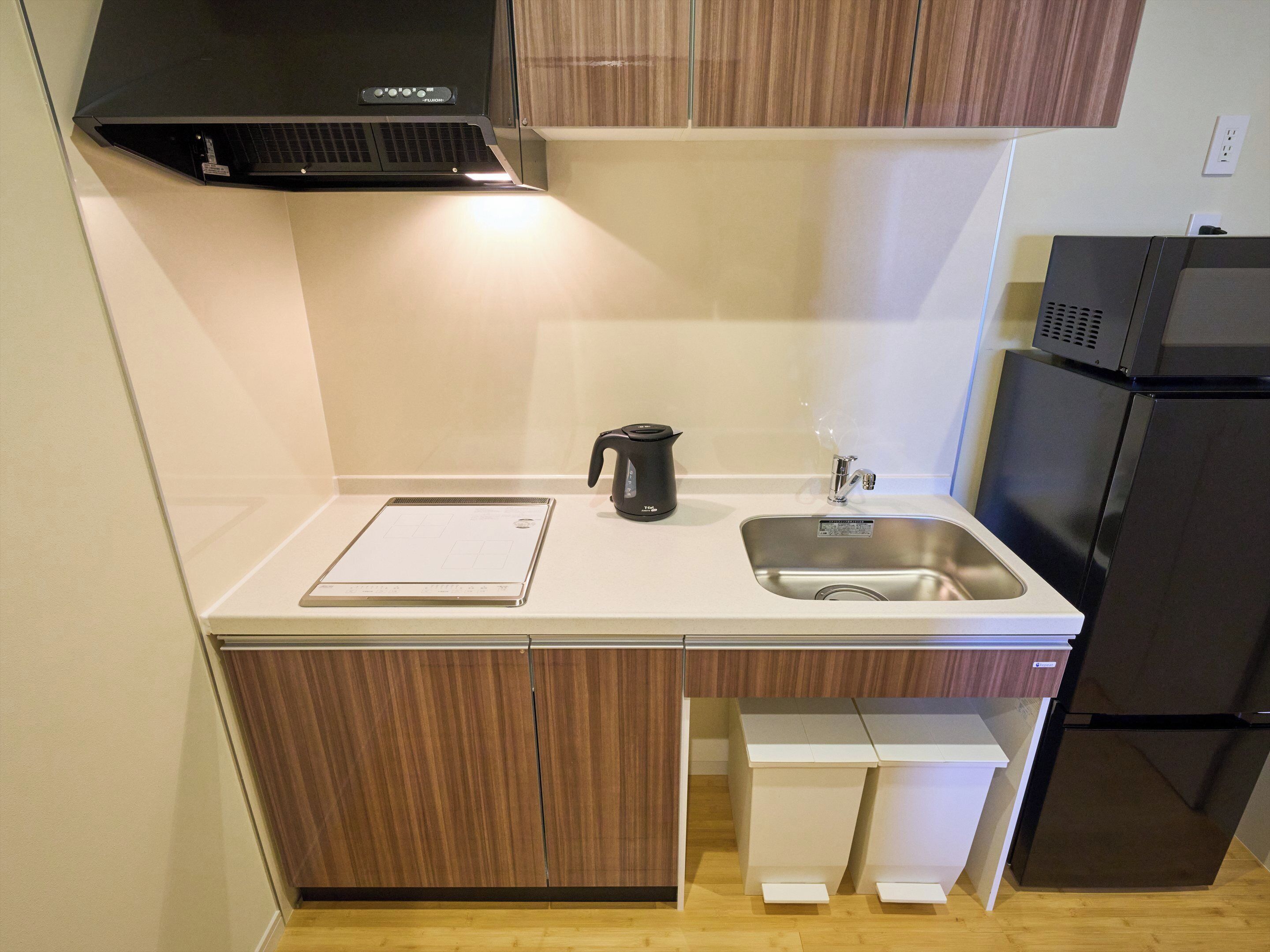 A compact kitchen with a stainless steel sink, a black kettle, and a microwave.