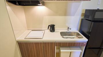 A compact kitchen with a stainless steel sink, a black kettle, and a microwave.