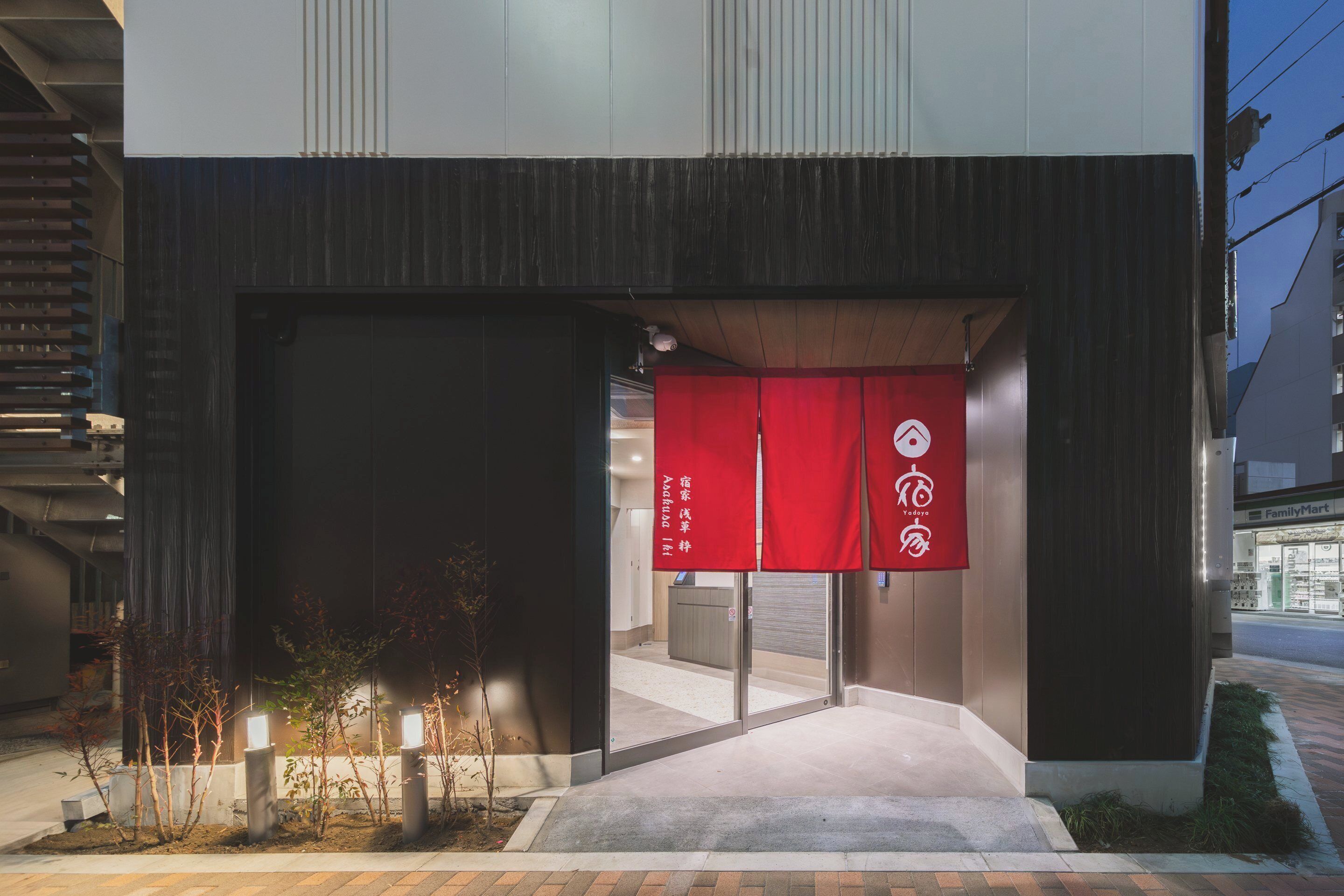 Entrada de un edificio moderno con un cartel rojo, un mostrador de recepción visible y un camino que conduce a la entrada.