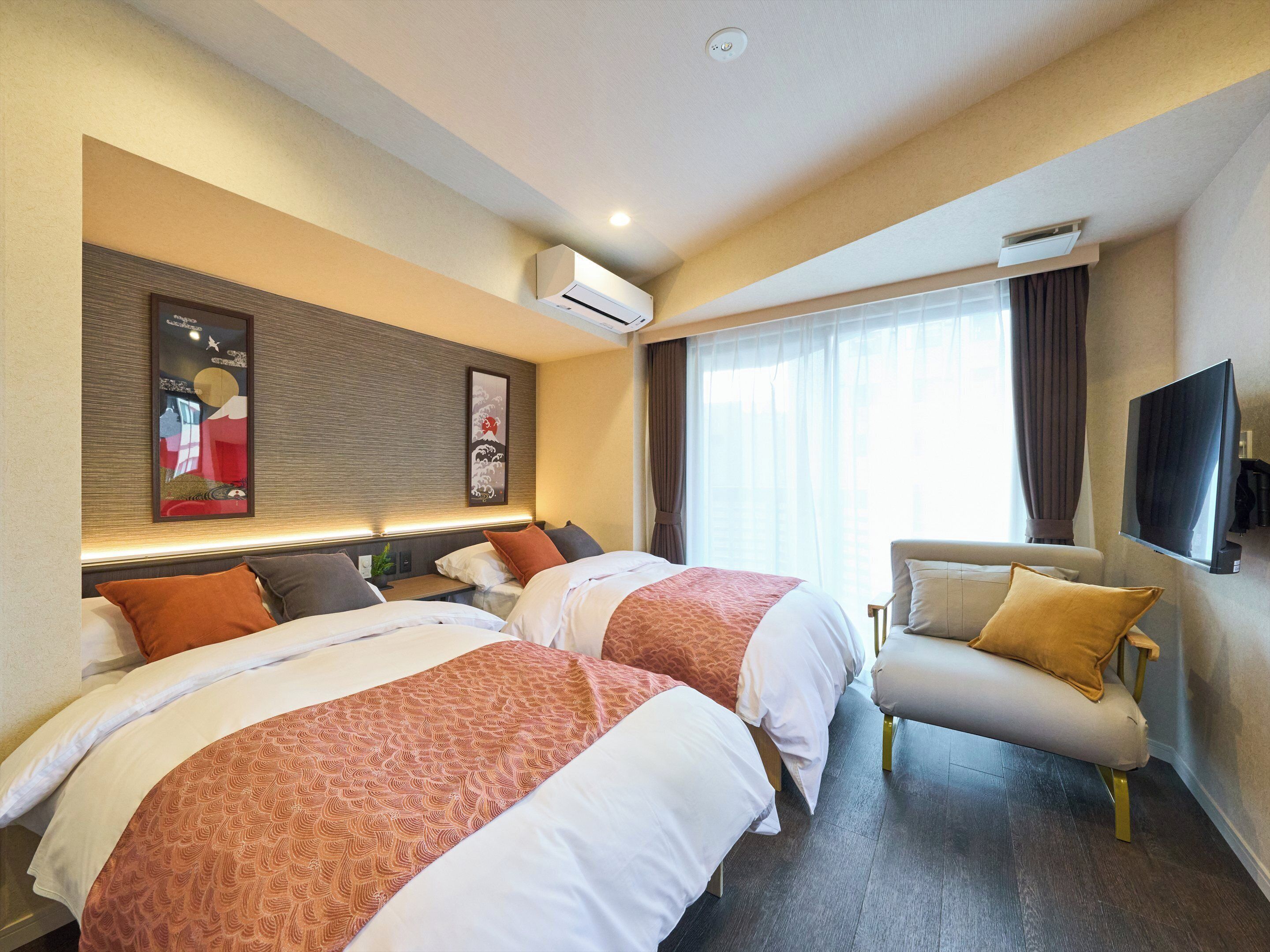 A hotel room with two beds, a sofa, a flat-screen TV, and a large window with curtains.