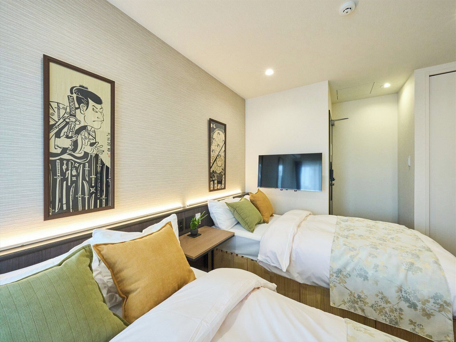 A hotel room with two beds, a bedside table, a TV, and artwork on the walls.