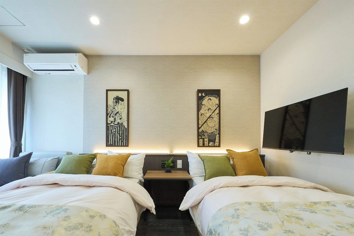 A hotel room with two beds, a flat-screen TV, an air conditioner, and artwork on the wall.