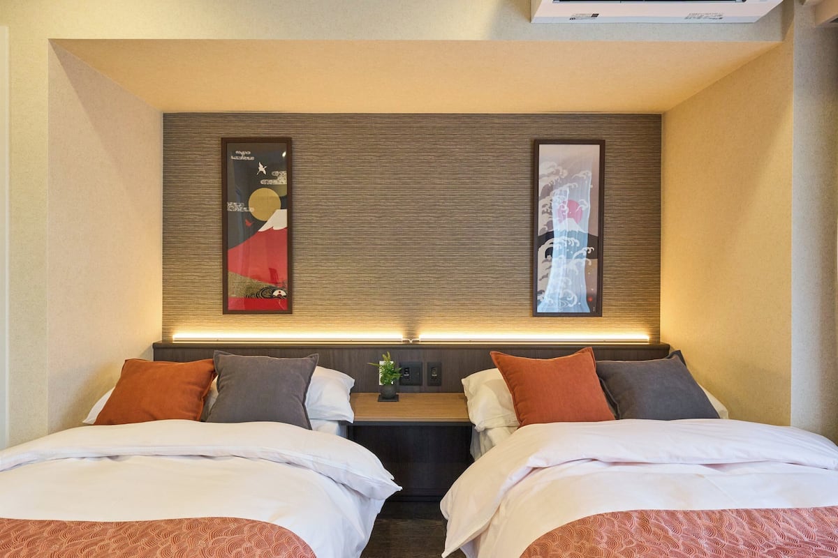 A hotel room with two beds, a nightstand, and two framed artworks on the wall.