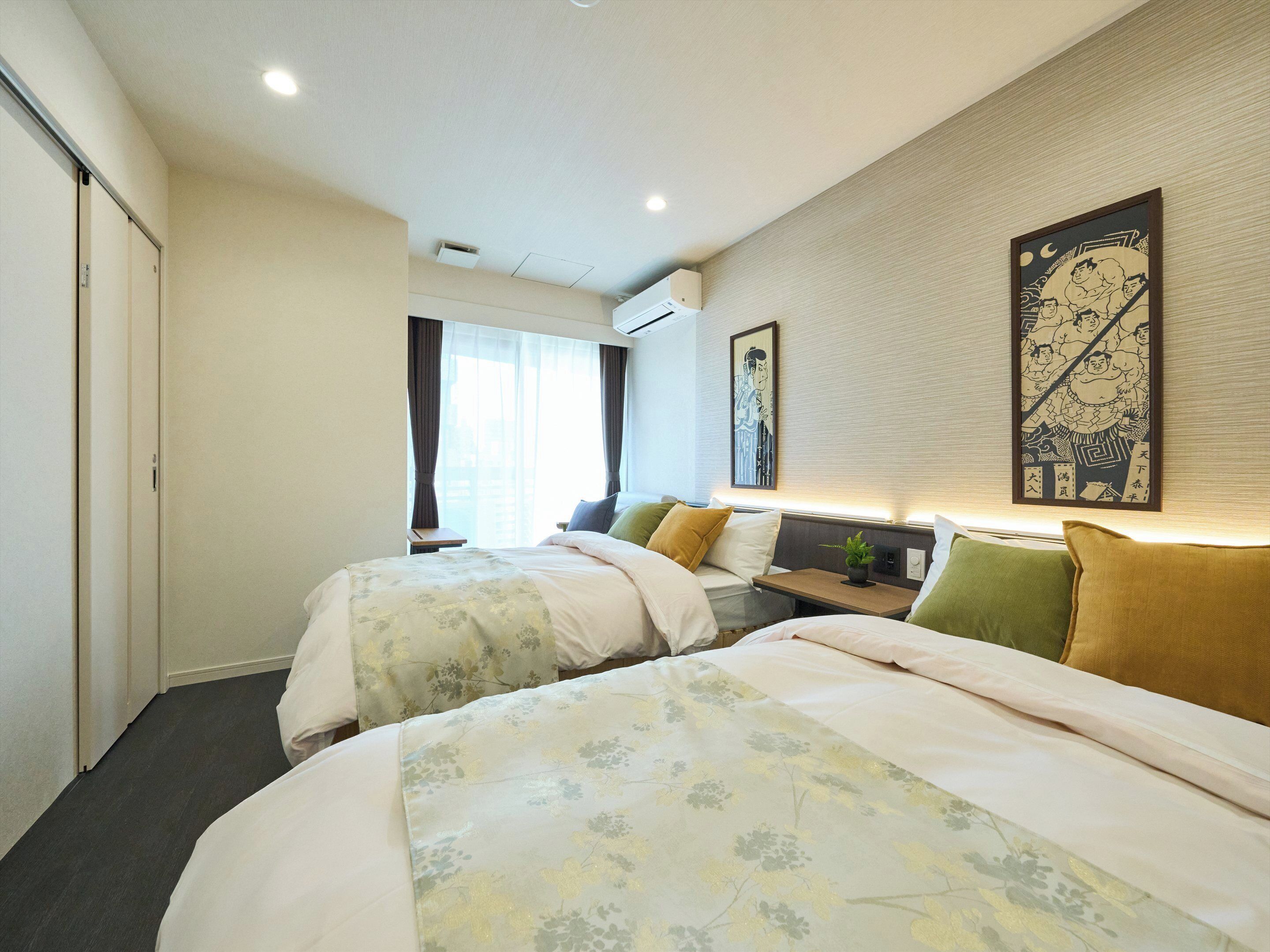 Ein Hotelzimmer mit zwei Betten, einem kleinen Tisch, einem an der Wand befestigten Fernseher und einem Fenster mit Vorhängen.