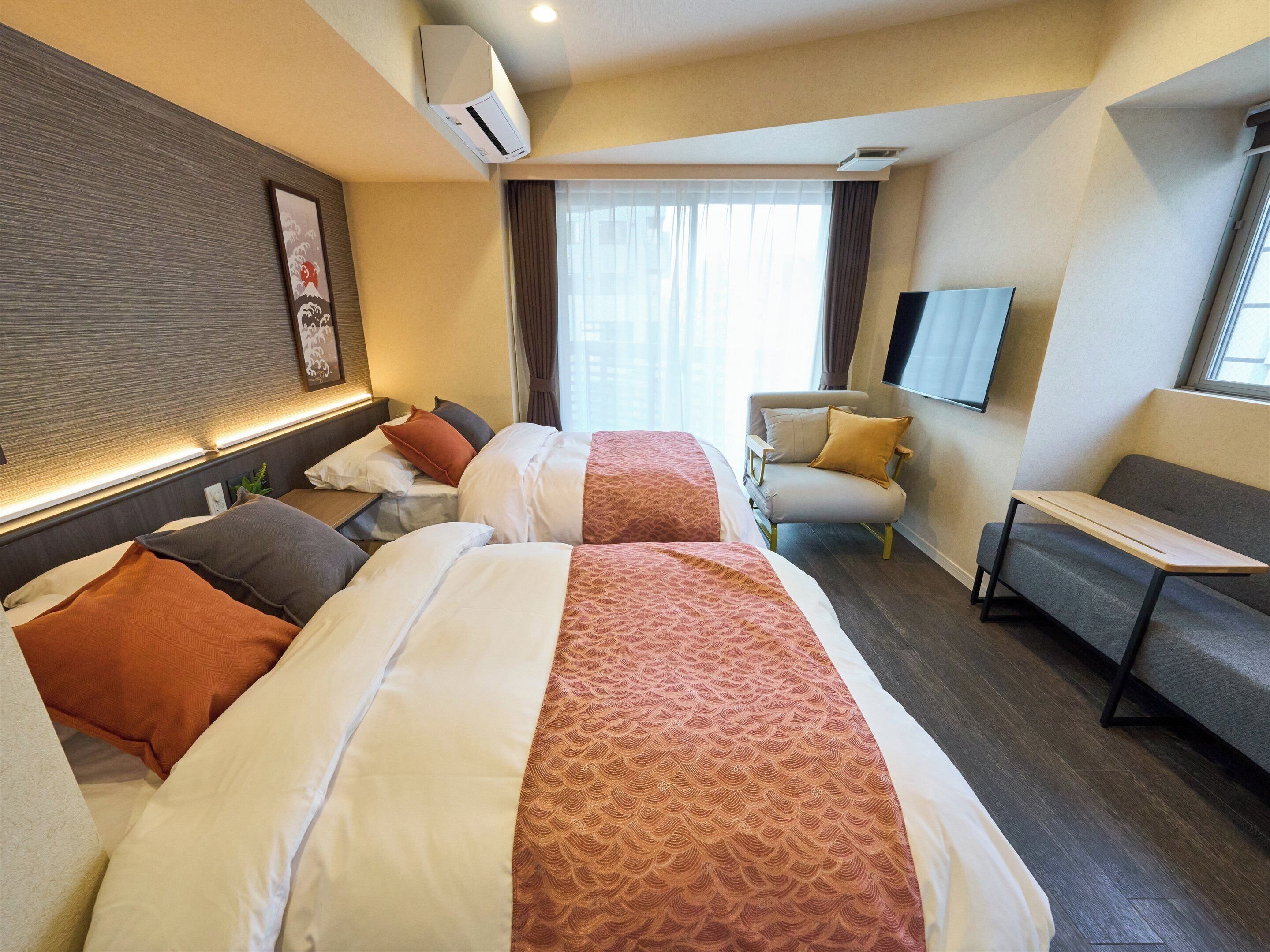 Una habitación de hotel con dos camas, un sofá, un televisor y un equipo de aire acondicionado.