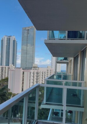 A high-rise building with a glass facade, adjacent residential buildings, and a balcony with a railing. - 2B Appartment Synny islas (Sunny Isles Beach)