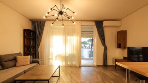 A modern living room with a sofa, a coffee table, a TV, and a wooden cabinet. - Designer Apartment in the Pines San Pietro (Ishëm)
