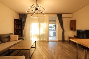 A modern living room with a sofa, a coffee table, a TV, and a wooden cabinet. - Designer Apartment in the Pines San Pietro (Ishëm)