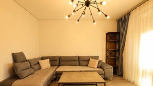 A modern living room with a sectional sofa, a coffee table, and a ceiling light fixture. - Designer Apartment in the Pines San Pietro (Ishëm)