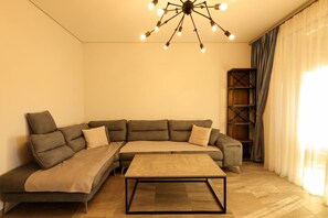 A modern living room with a sectional sofa, a coffee table, and a ceiling light fixture. - Designer Apartment in the Pines San Pietro (Ishëm)