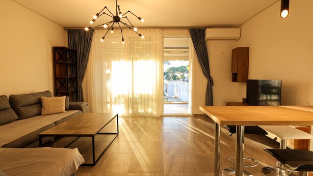A modern living room with a sofa, a coffee table, a TV, and a dining area. - Designer Apartment in the Pines San Pietro (Ishëm)