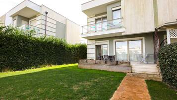 A modern two-story residential building with a flat roof, large windows, and a balcony with glass railings.